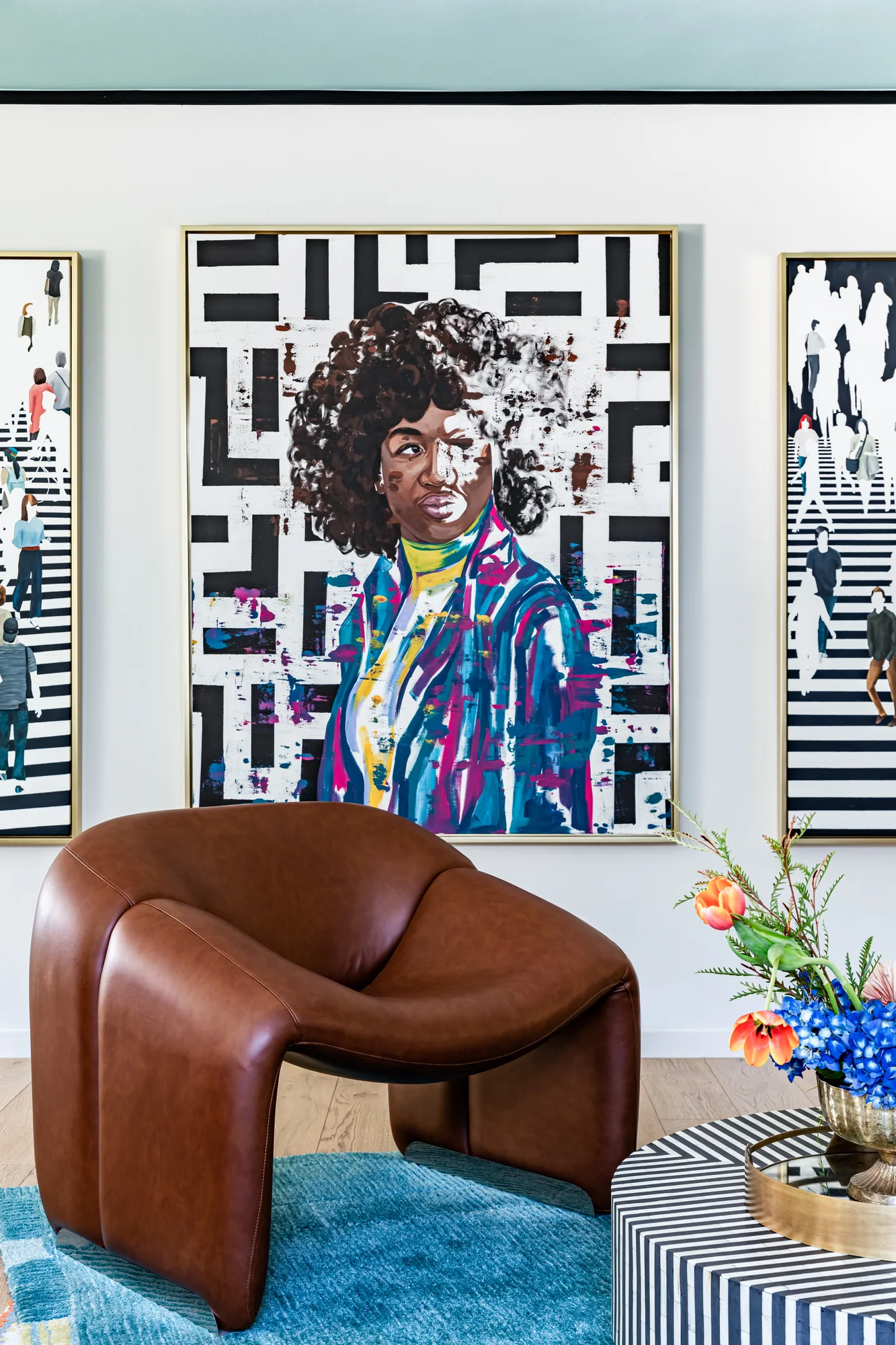 Bold portrait canvases above a sculptural tan leather chair