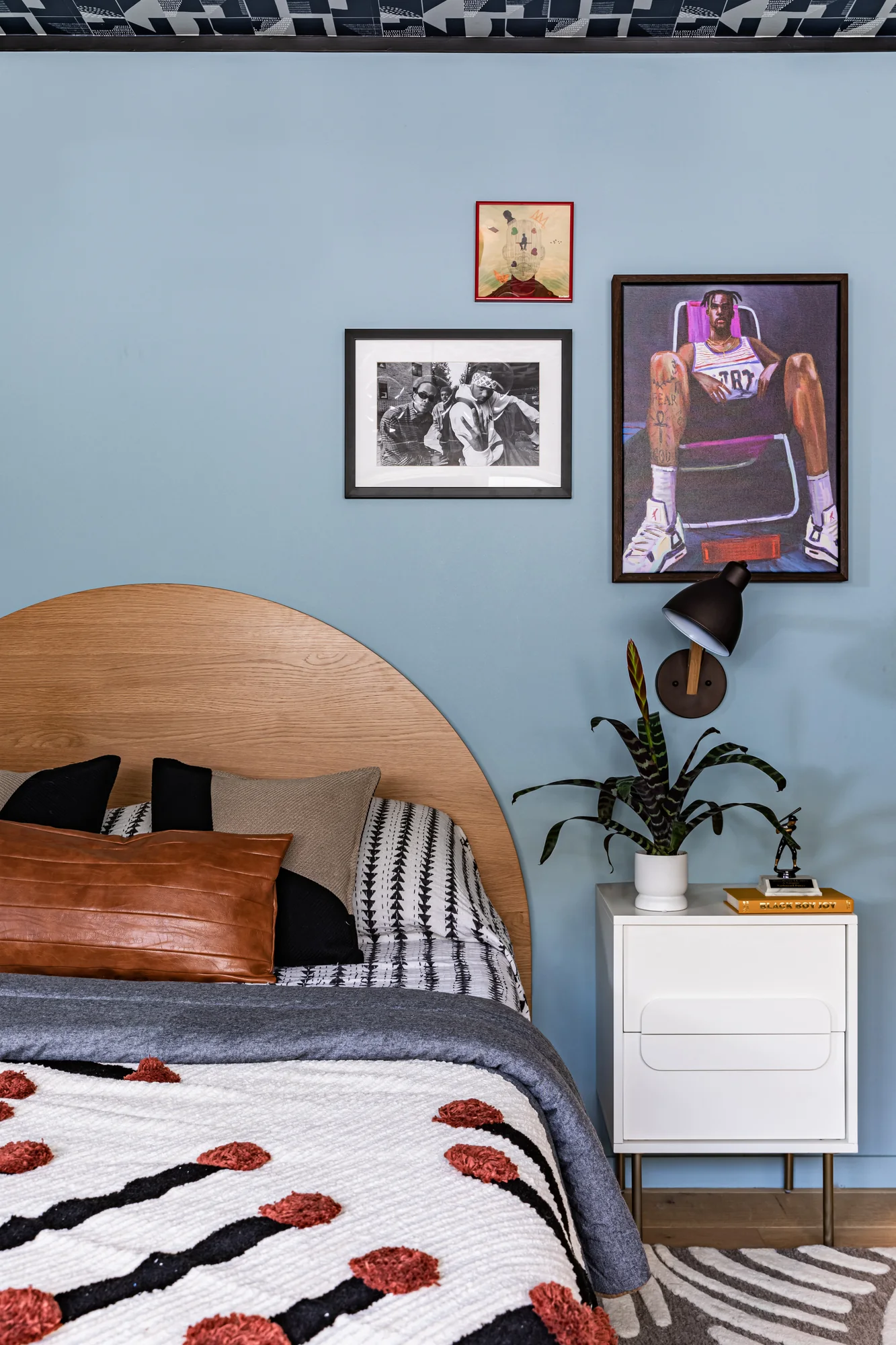 Arched wood headboard in a pale blue room hung with photography