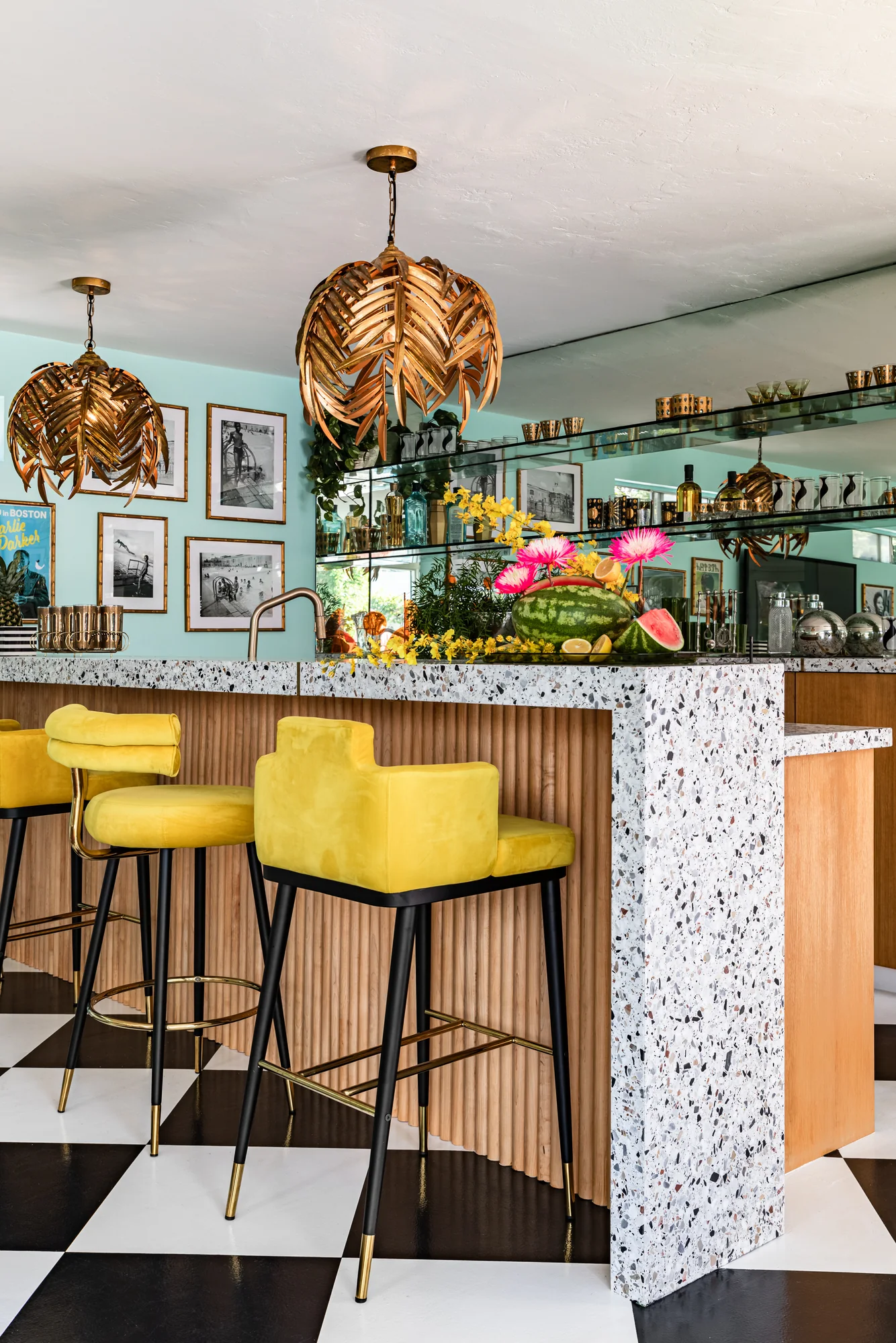 Pool-house bar with terrazzo counter, yellow stools and gilt palm pendants