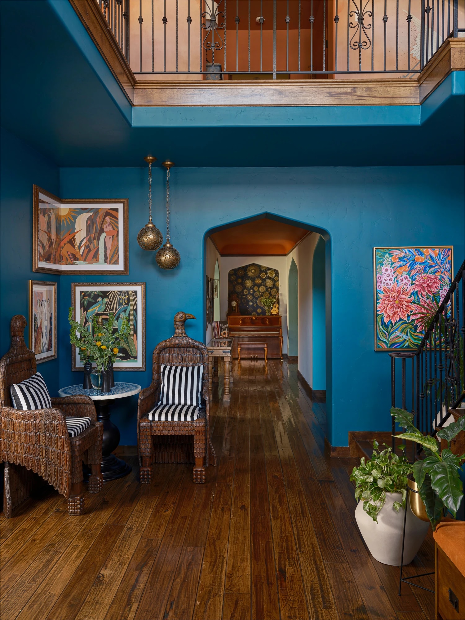 The double-height teal hall, hung with art and brass lanterns, looking through to the arched doorways beyond