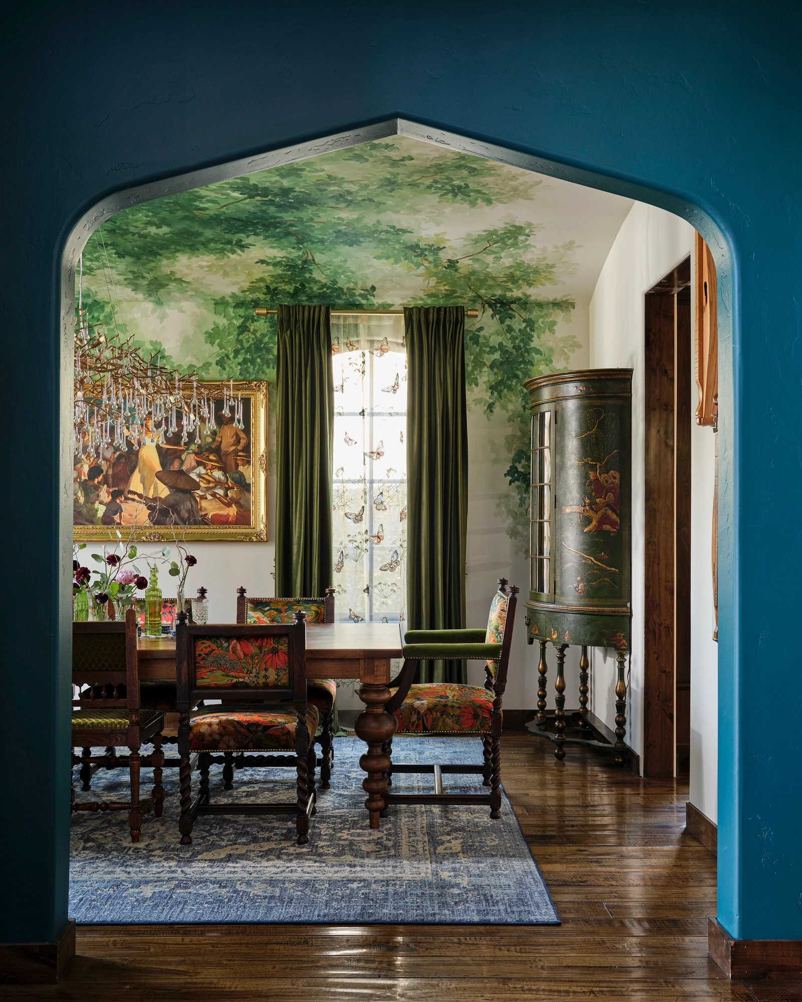 A teal archway opening onto the dining room, its ceiling painted with green foliage