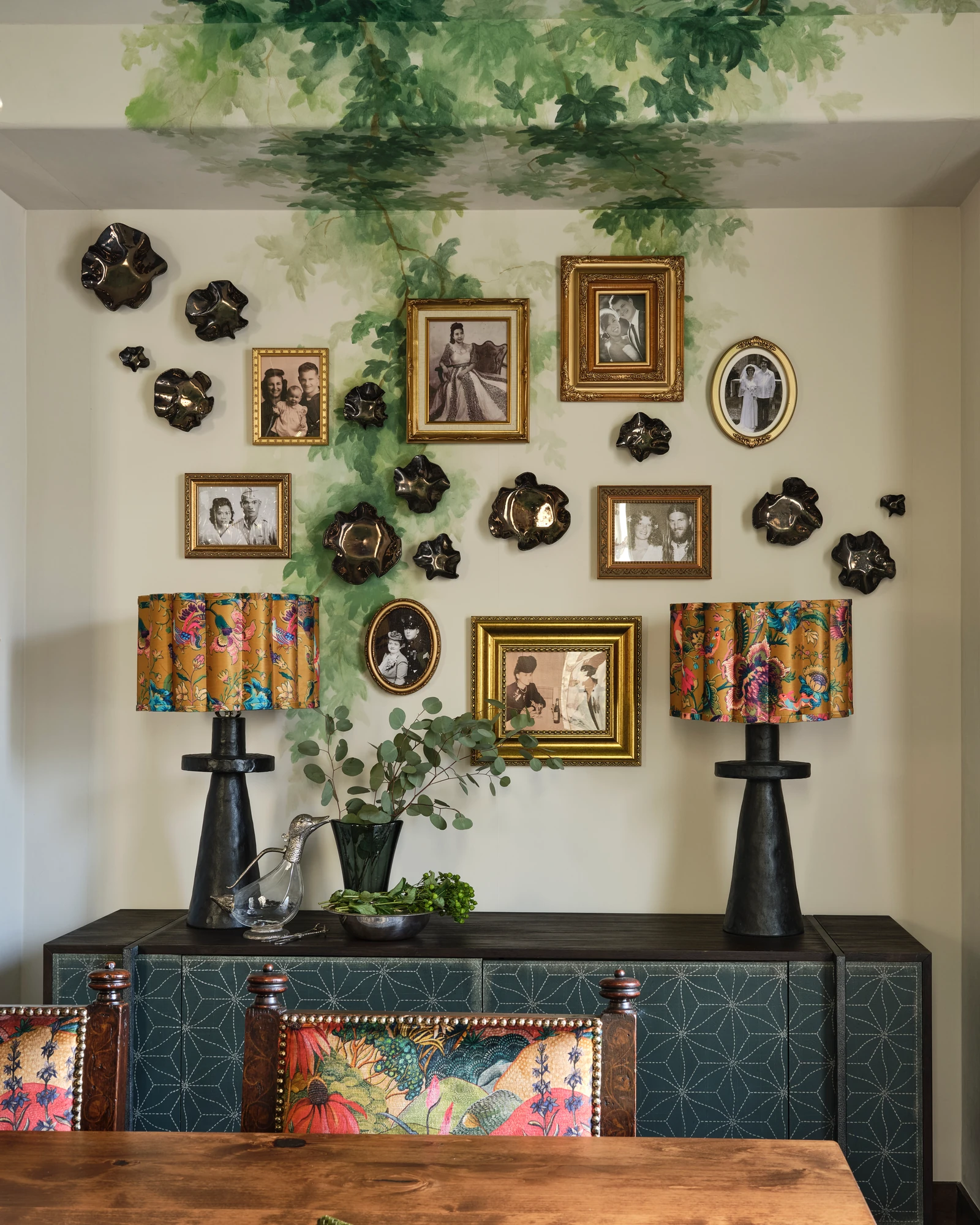 A salon wall of gilt portraits and black ceramic plates above a painted console