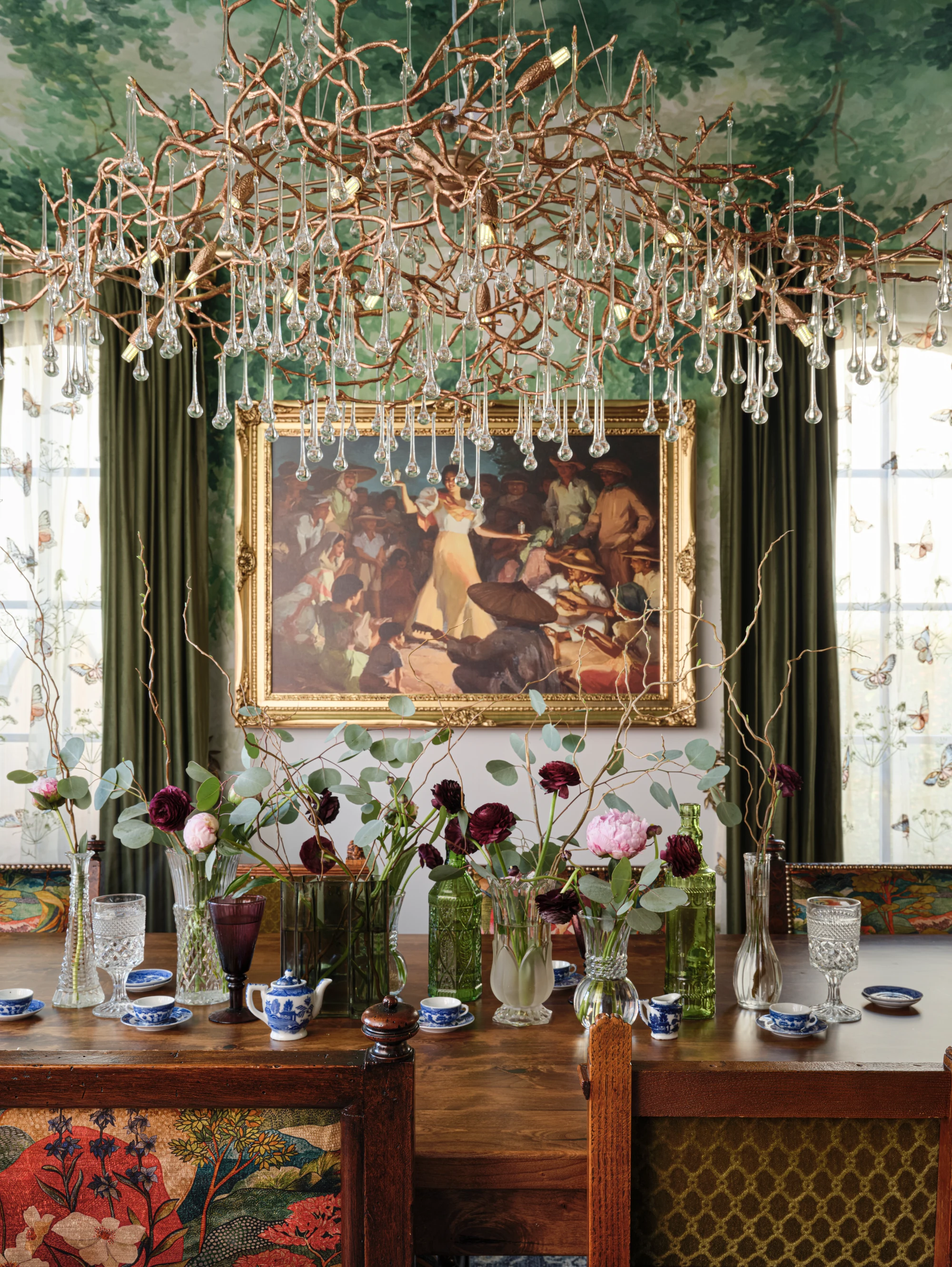 The Animal House dining room: a large narrative painting above a sideboard of flowers and china, under a chandelier of crystal droplets