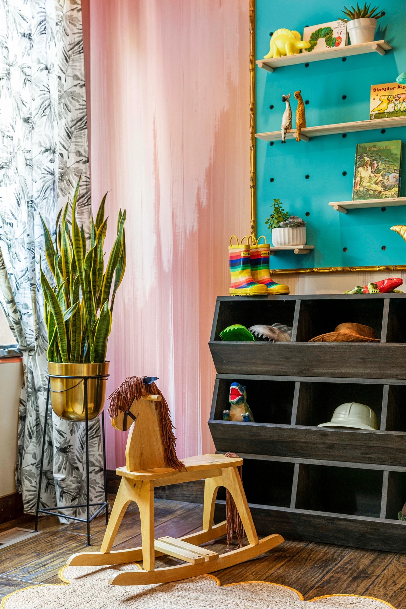 A wooden rocking horse in front of the teal pegboard and the toy cubbies