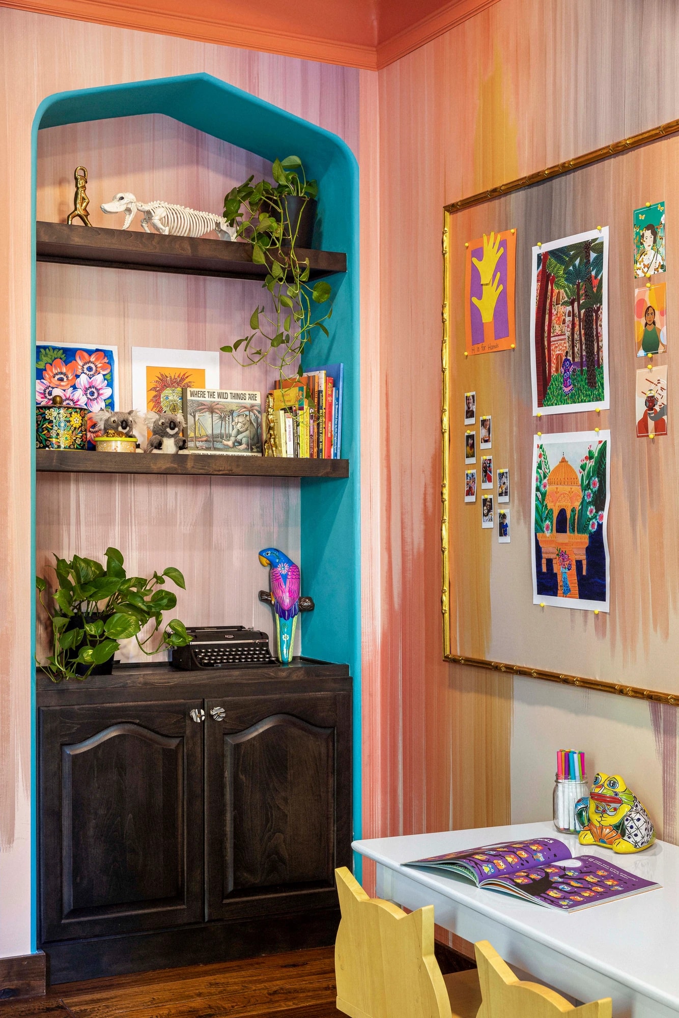 The arched teal shelving nook of books and toys beside the art table
