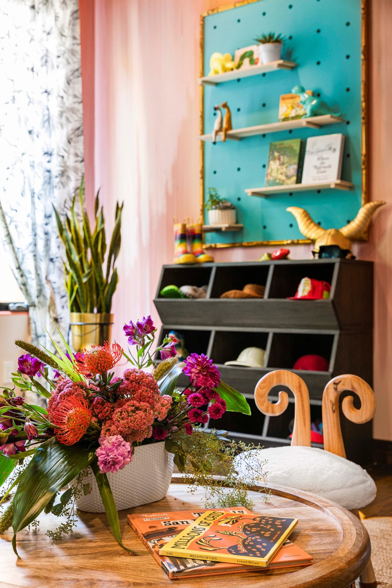 Flowers on a carved table in front of the teal pegboard shelving