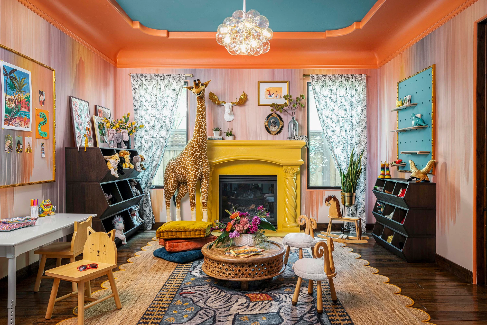 The playroom in full: coral walls, a canary-yellow fireplace, a life-size giraffe, toy cubbies and a scalloped rug
