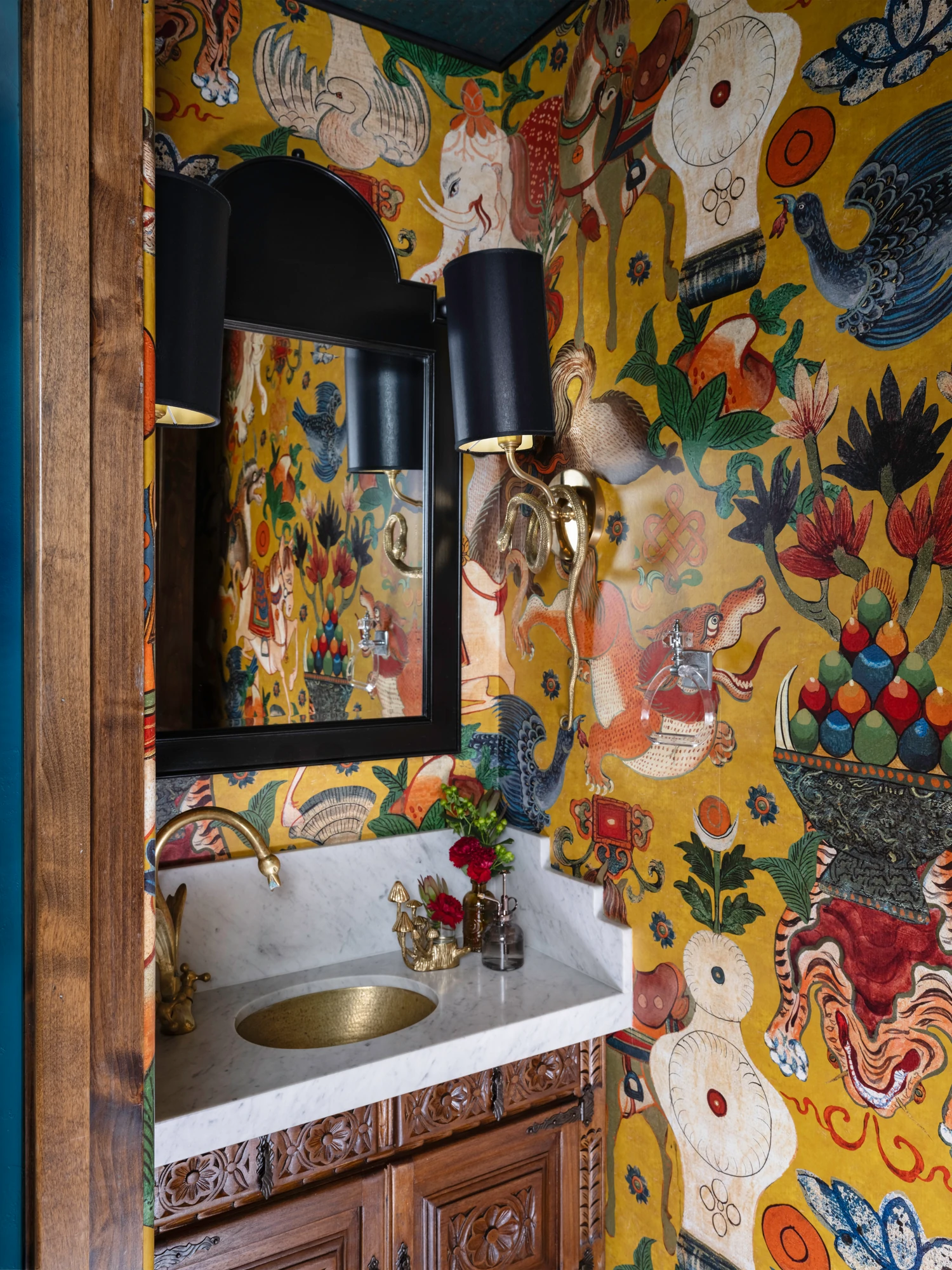 The powder room papered in bold yellow florals, with a brass basin and a black sconce