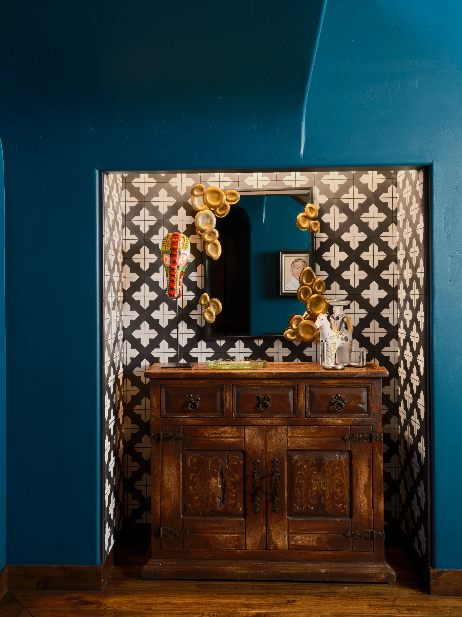 A carved wooden cabinet set into a lattice-tiled alcove against a deep teal wall