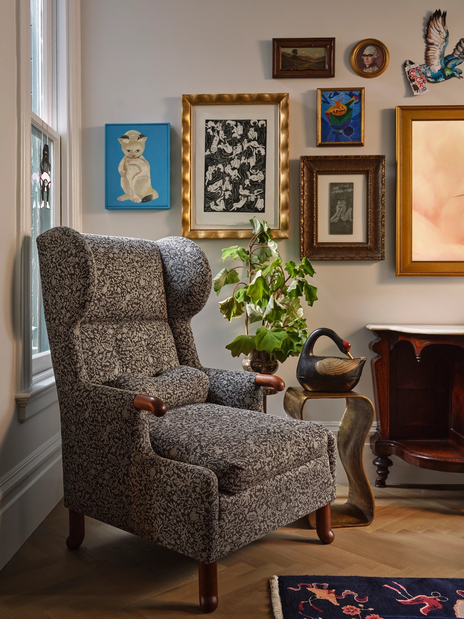 Wing chair below a salon hang of framed art