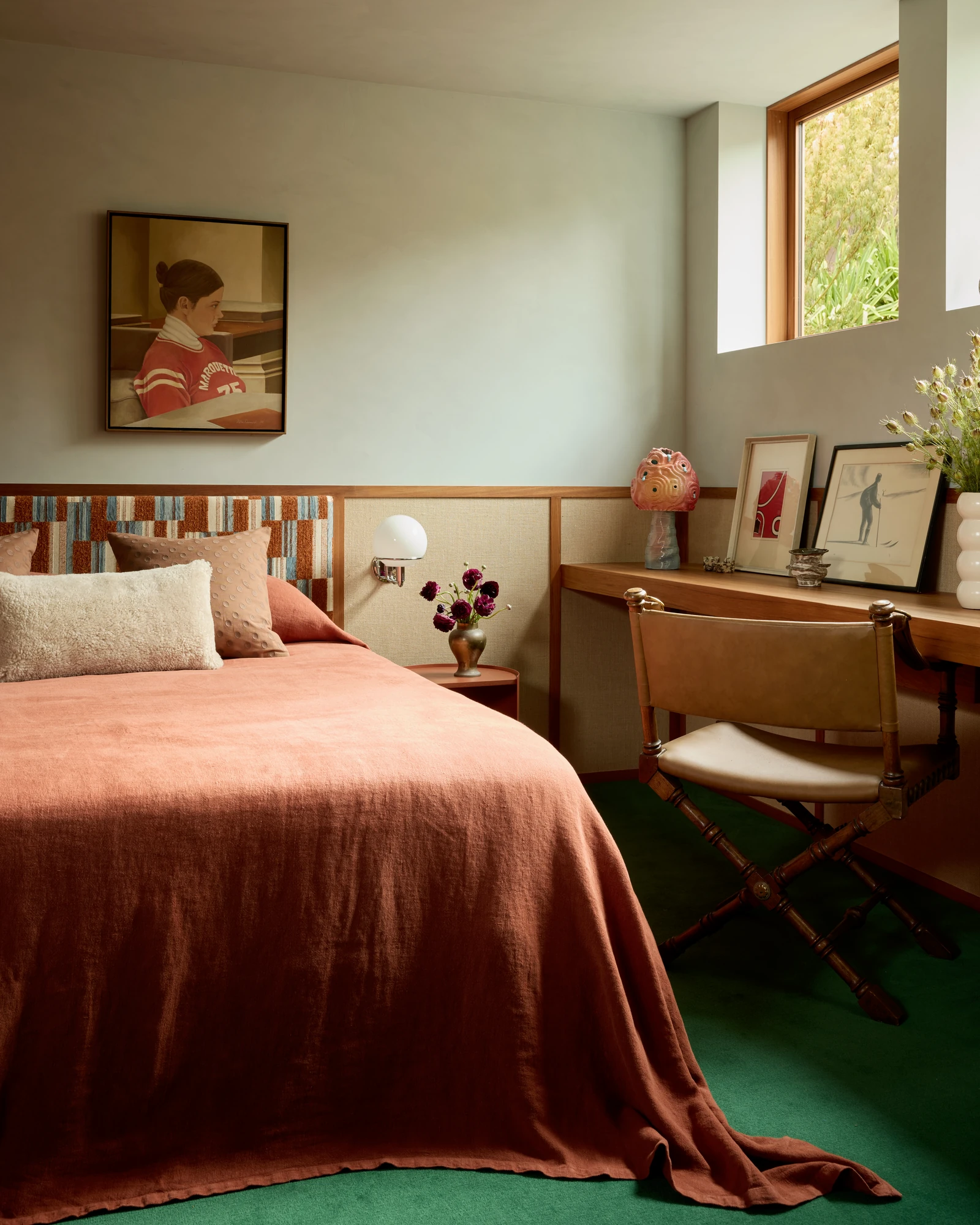 Guest bedroom with a rust bedspread over green carpet and a corner desk