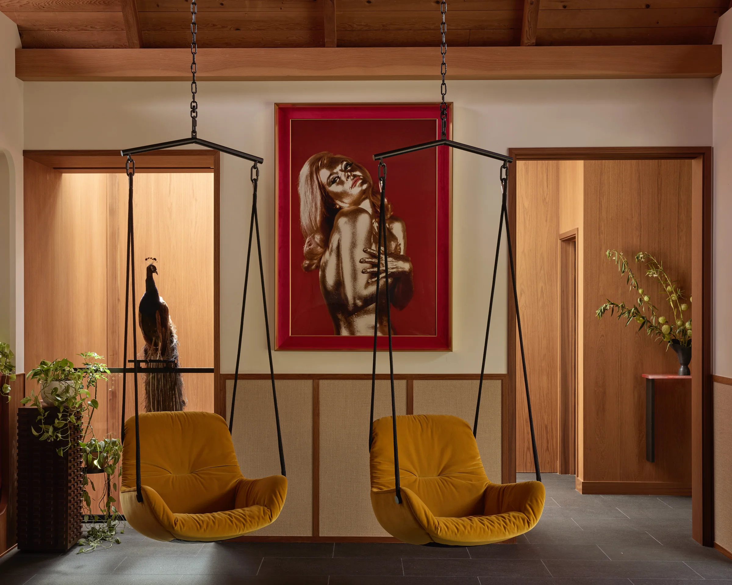 Entry lounge with two hanging rattan swing chairs beneath a red-framed portrait