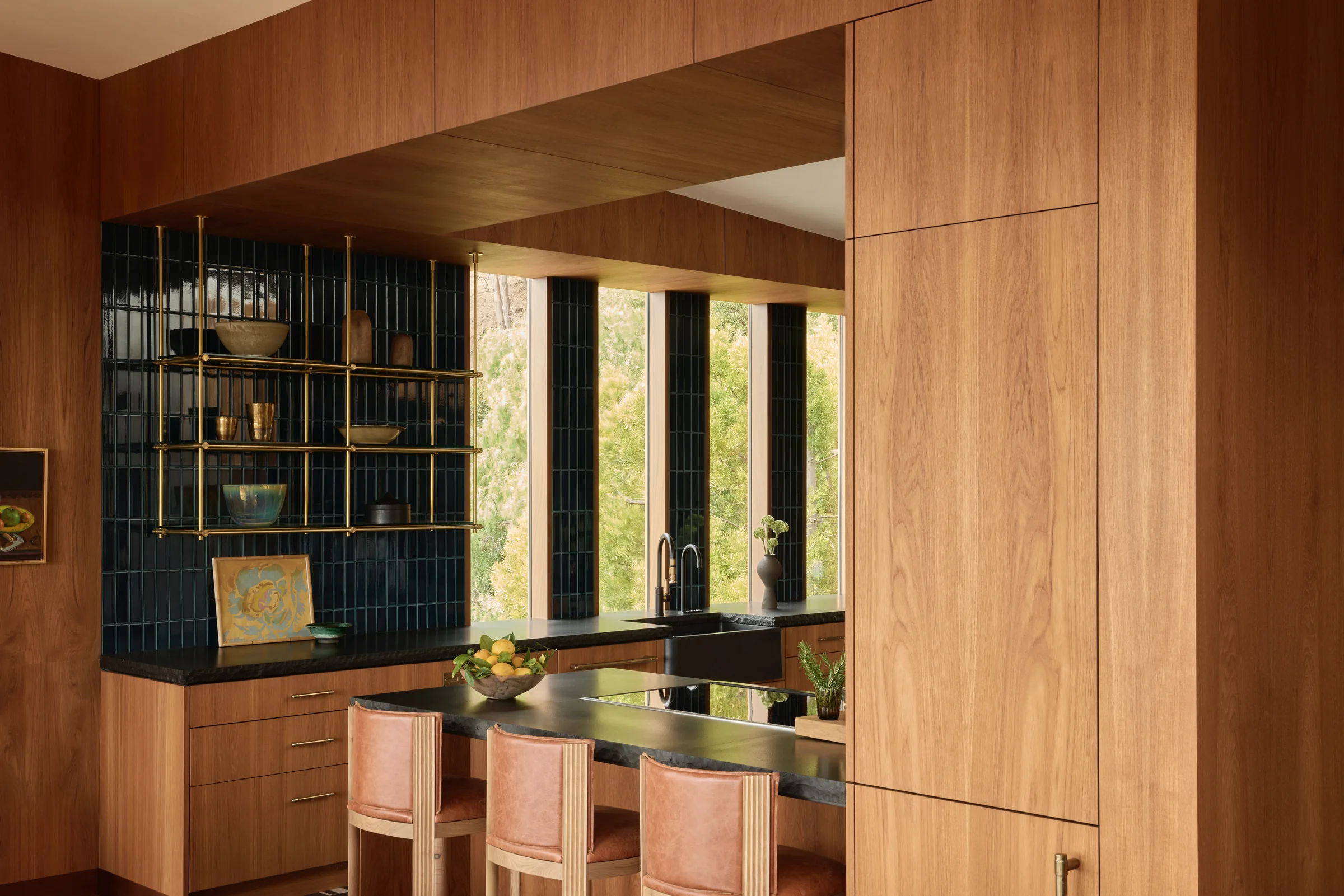 Kitchen with brass shelving over deep blue tile and a black stone counter