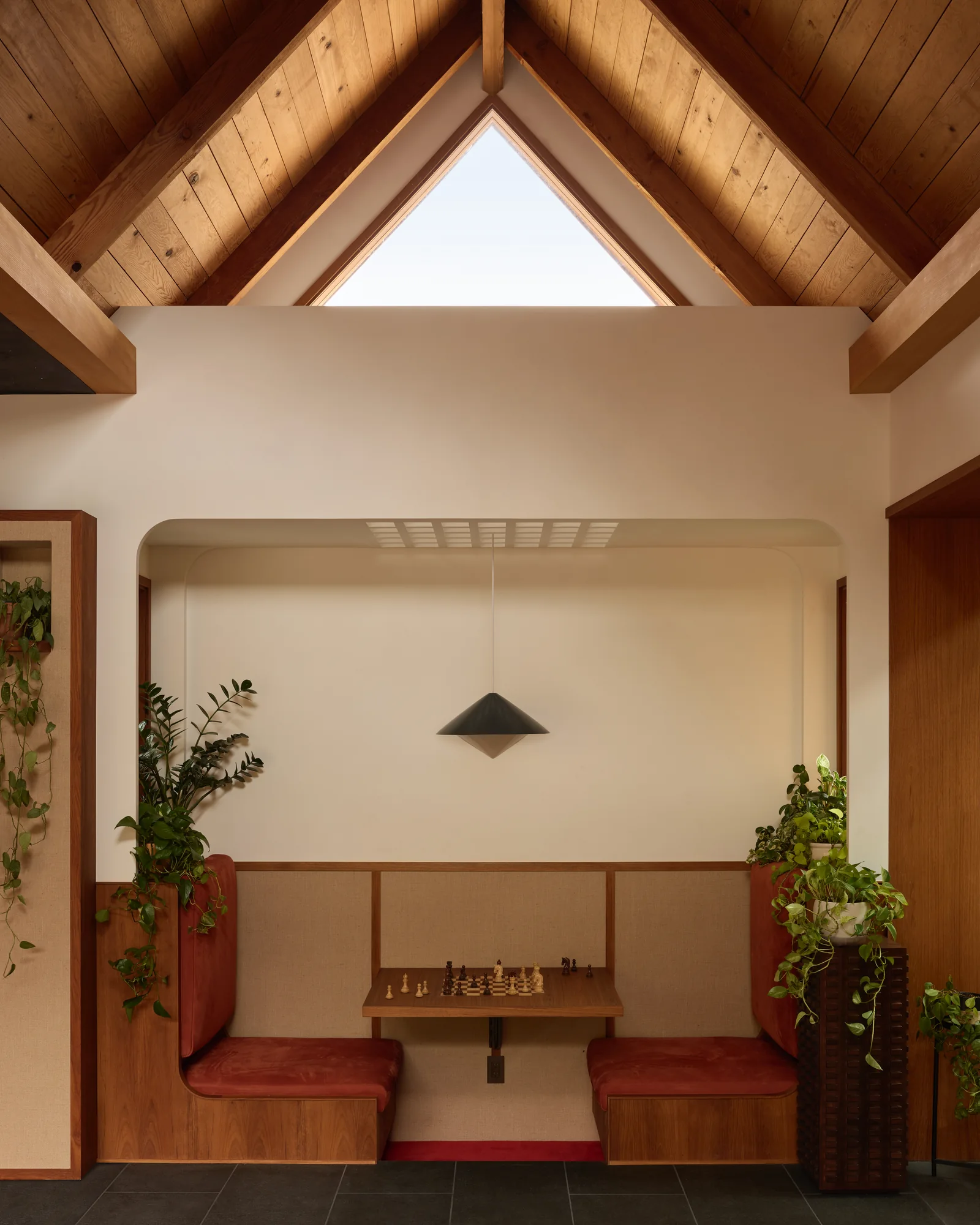 Triangular clerestory window above a red banquette nook